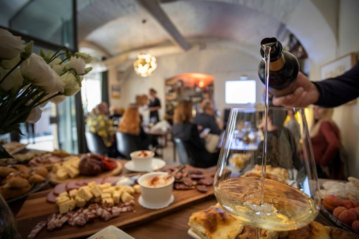 Image of Graševina wine poured in the glass, in the background beautifully served table full of Slavonian delicacies 