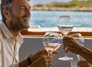 Image of friend laughing while enjoying rose wine by the sea