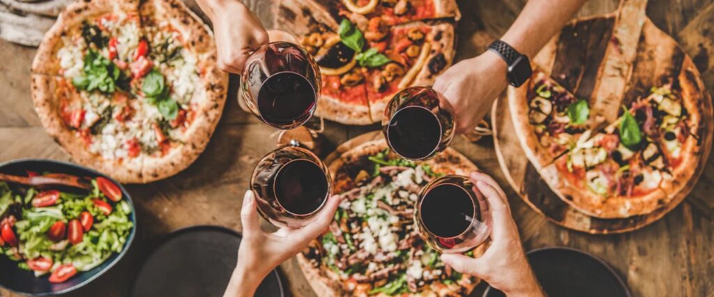 Image of friends with glasses of red wine cheering over pizza