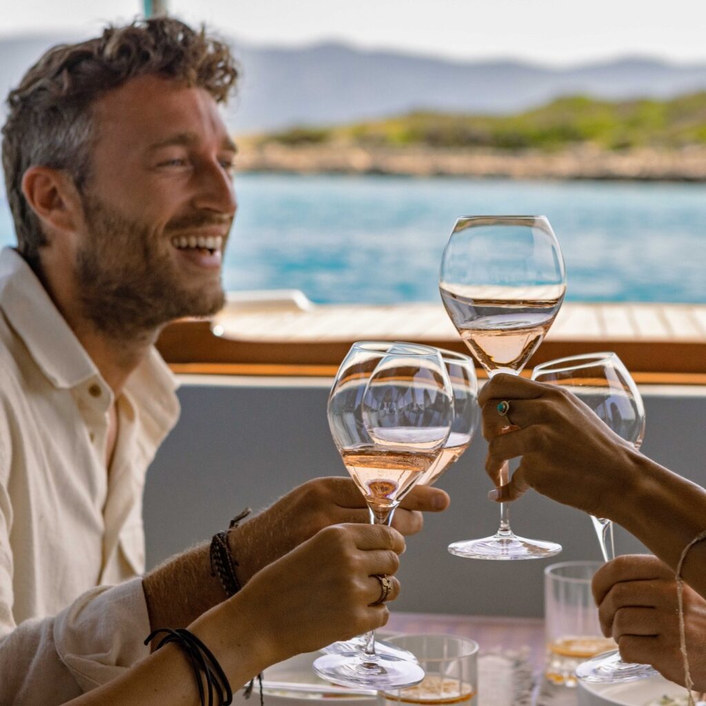 Image of friend laughing while enjoying rose wine by the sea