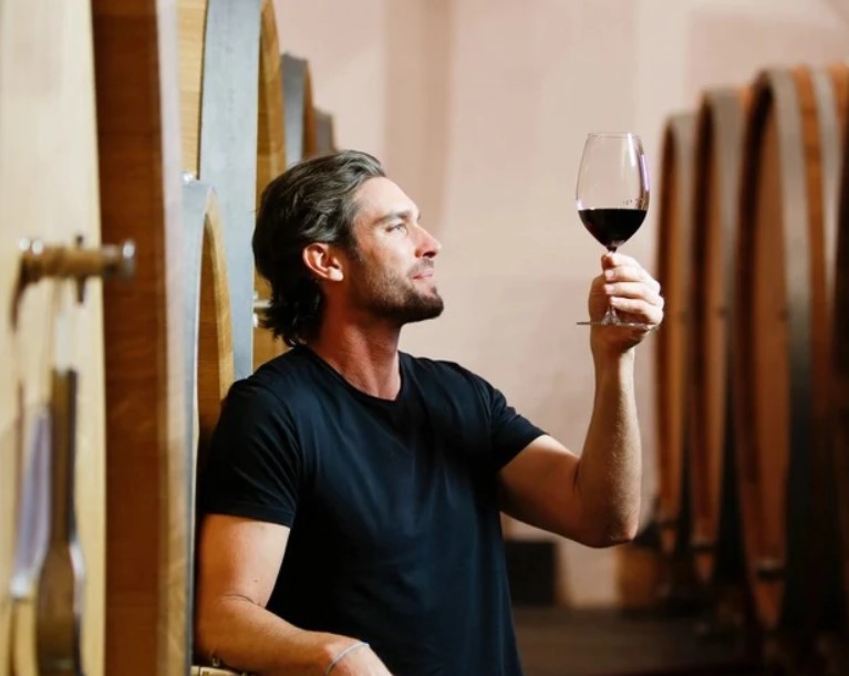 Image of a man in the wine cellar observing a glass of red wine