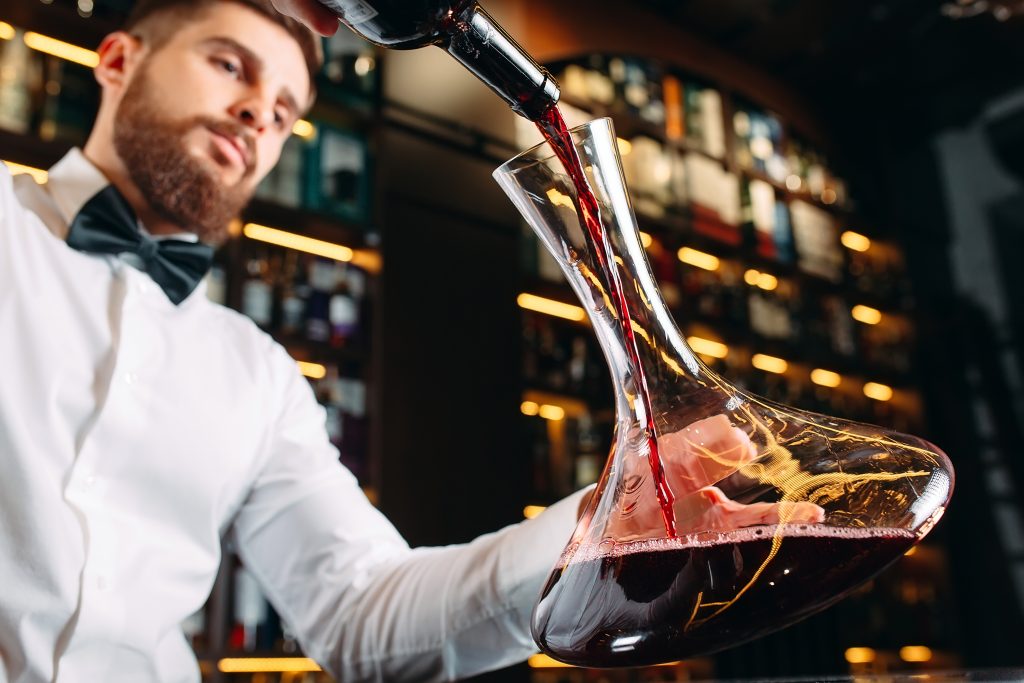 Image of waiter pouring red wine in a wine decanter