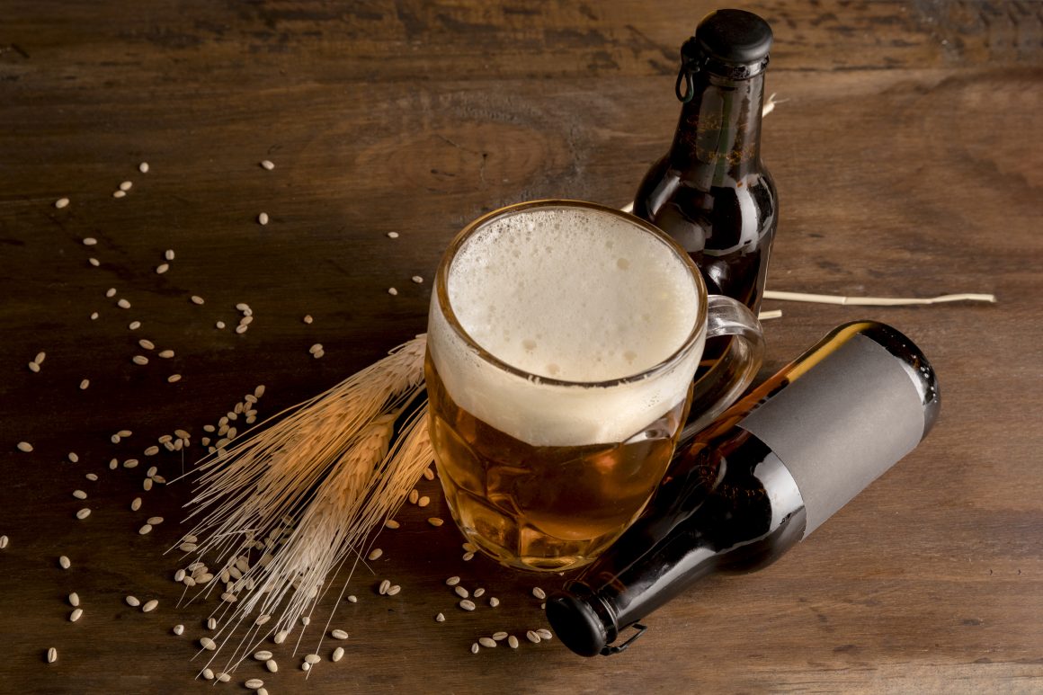 Image of a glass of wheat beer with brown bottles of beer on wooden table